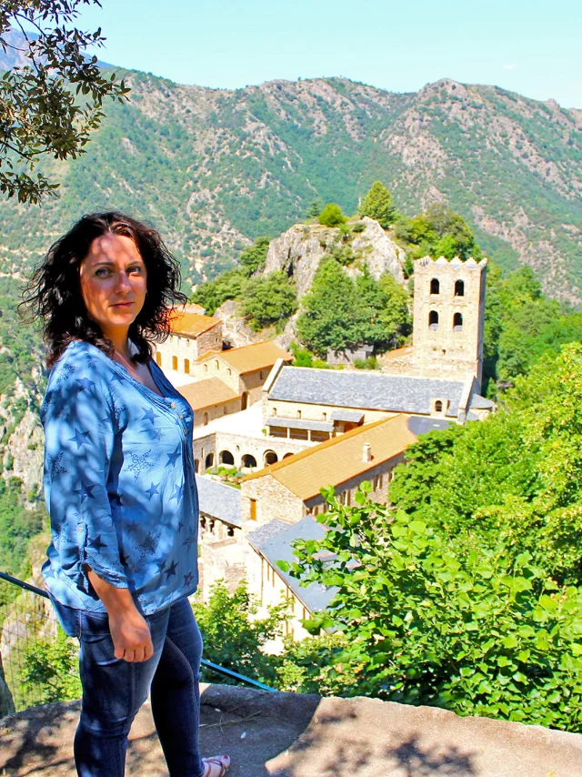 Personne admirant la vue sur l’abbaye Saint-Martin du Canigou, perchée sur son éperon rocheux au cœur des montagnes verdoyantes.