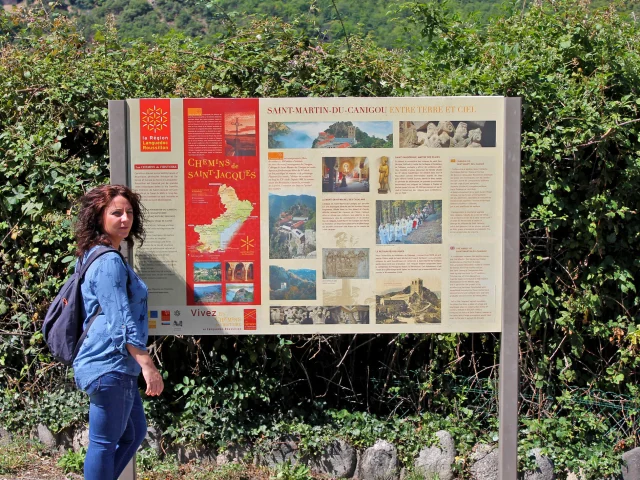Personne lisant un panneau d’information touristique sur l’abbaye Saint-Martin du Canigou et les chemins de Saint-Jacques-de-Compostelle.