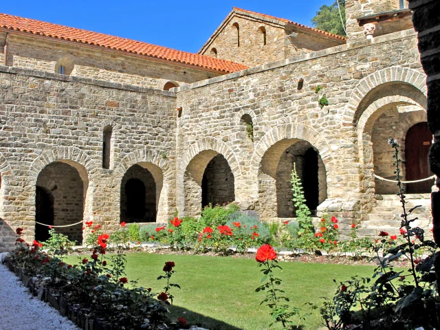 Cloître roman de l’abbaye Saint-Martin du Canigou, avec ses arcades en pierre et son jardin orné de roses rouges.
