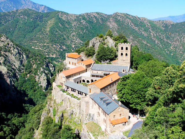 Vue aérienne de l’abbaye Saint-Martin du Canigou, perchée sur un éperon rocheux au cœur des montagnes verdoyantes.