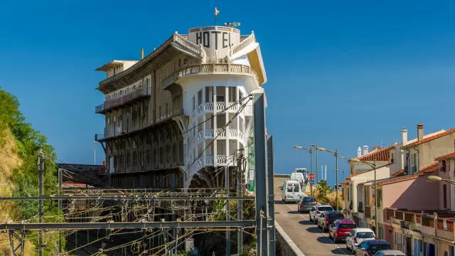 Vue sur l’hôtel du Belvédère du Rayon Vert, imposant bâtiment Art déco dominant les voies ferrées et la mer à Cerbère, sous un ciel bleu limpide.
