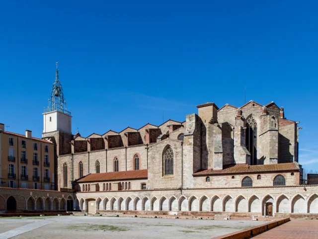 Vue du cloître du Campo Santo et de la cathédrale Saint-Jean-Baptiste de Perpignan sous un ciel bleu.