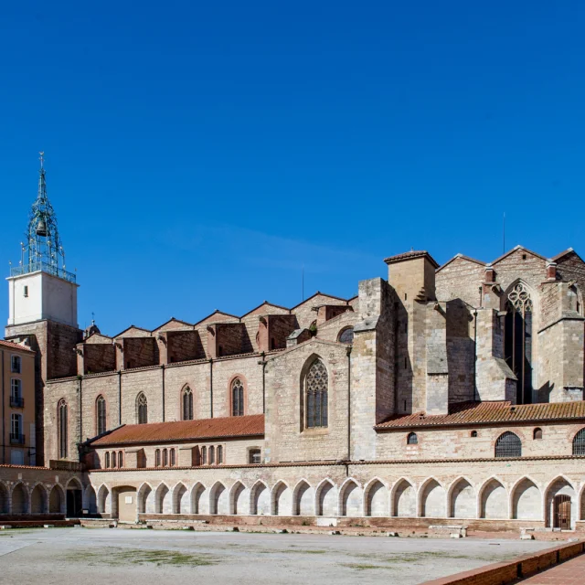 Vue du cloître du Campo Santo et de la cathédrale Saint-Jean-Baptiste de Perpignan sous un ciel bleu.
