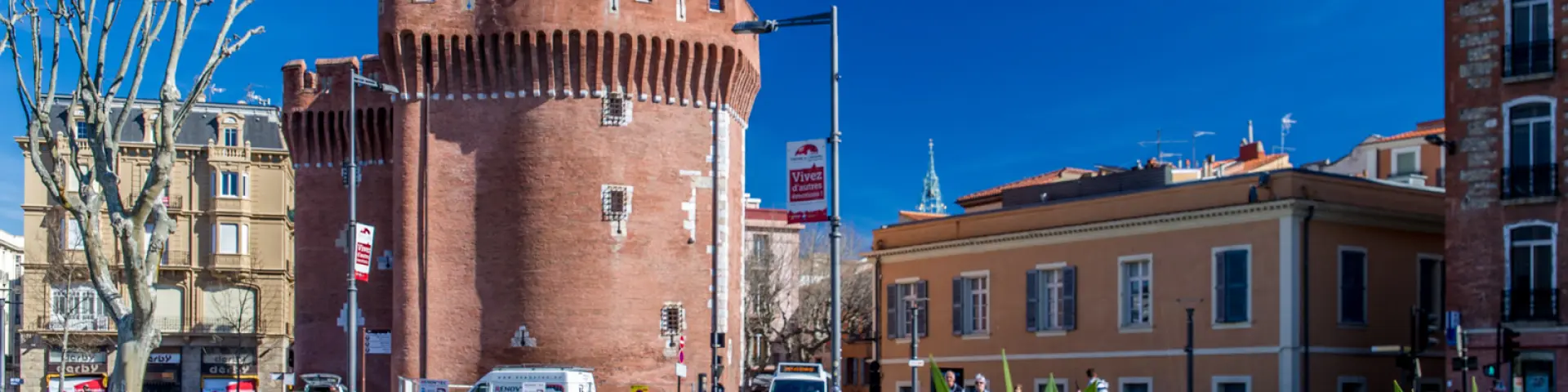 Le Castillet de Perpignan, monument en briques rouges surmonté du drapeau catalan, sous un ciel bleu.
