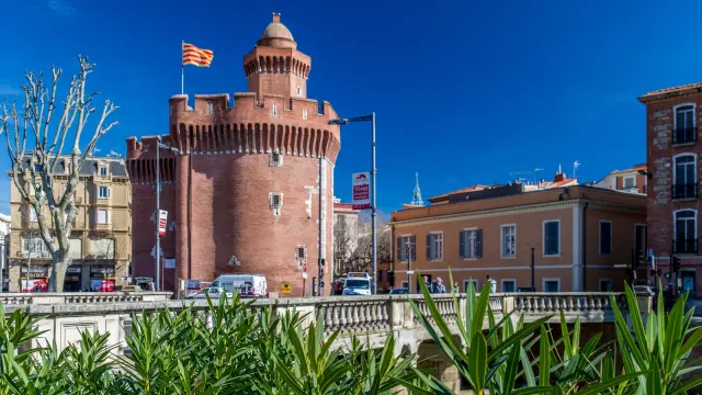 Le Castillet de Perpignan, monument en briques rouges surmonté du drapeau catalan, sous un ciel bleu.