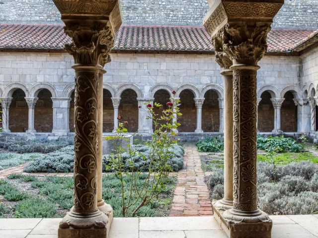 Vue du cloître roman avec ses colonnes sculptées et son jardin intérieur planté de lavandes et de rosiers.
