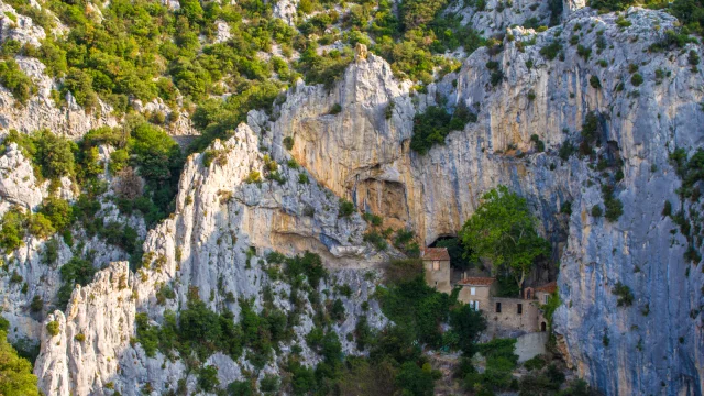 Vue de l’ermitage Saint-Antoine de Galamus, bâti à flanc de falaise dans les gorges, entouré de parois calcaires et de végétation verdoyante.