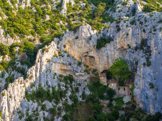 Vue de l’ermitage Saint-Antoine de Galamus, bâti à flanc de falaise dans les gorges, entouré de parois calcaires et de végétation verdoyante.