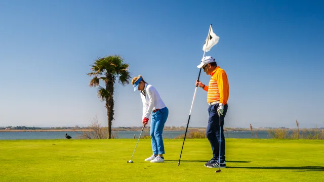 Deux golfeurs sur un green en bord de mer, sous un ciel bleu, l’un prêt à putter tandis que l’autre tient le drapeau du trou.