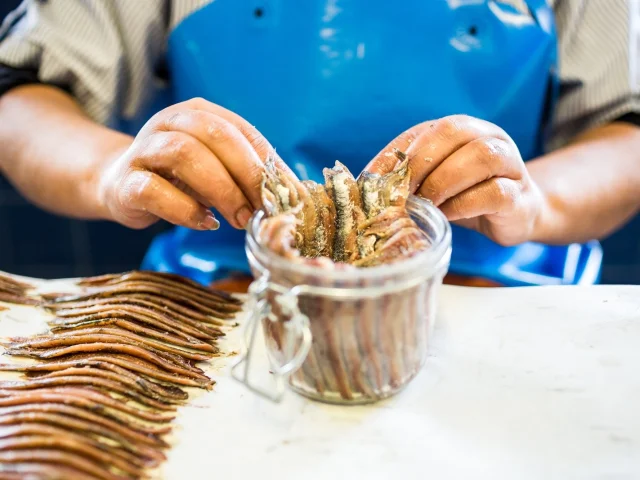Gros plan sur les mains d’un artisan disposant soigneusement des filets d’anchois dans un bocal en verre lors de la préparation traditionnelle à Collioure.