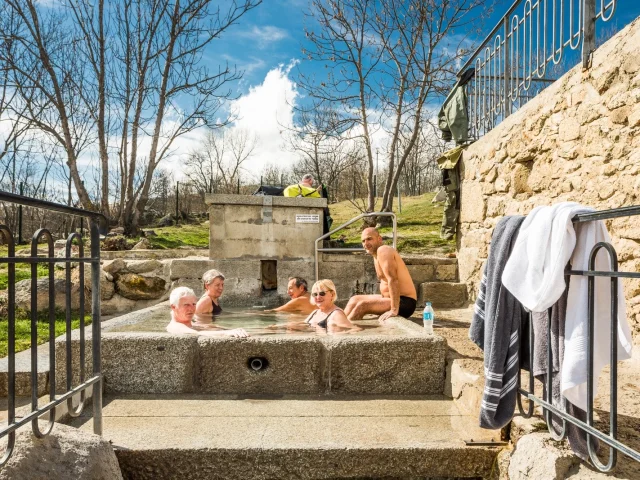 Groupe de personnes se relaxant dans le bassin d’eau chaude naturelle des bains de Dorres, en plein air sous un ciel ensoleillé.