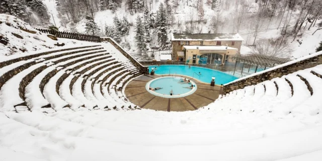 Vue en hauteur des bains de Saint-Thomas-les-Bains en hiver, avec des baigneurs profitant des bassins d’eau chaude naturelle entourés de neige.