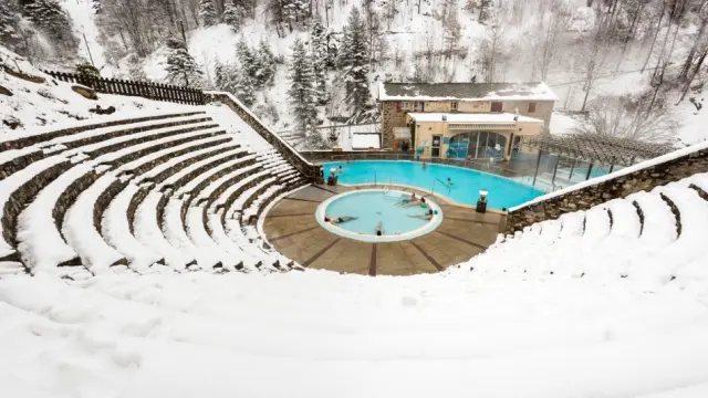 Vue en hauteur des bains de Saint-Thomas-les-Bains en hiver, avec des baigneurs profitant des bassins d’eau chaude naturelle entourés de neige.