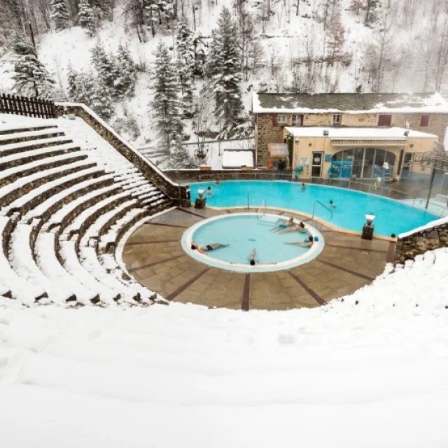Vue en hauteur des bains de Saint-Thomas-les-Bains en hiver, avec des baigneurs profitant des bassins d’eau chaude naturelle entourés de neige.