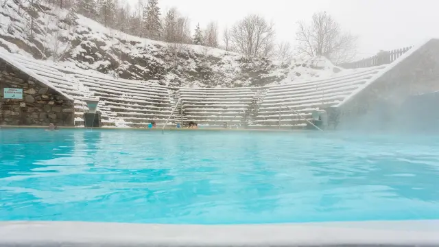 Bassin extérieur des bains de Saint-Thomas-les-Bains entouré de neige, avec des baigneurs profitant des eaux chaudes naturelles en hiver.