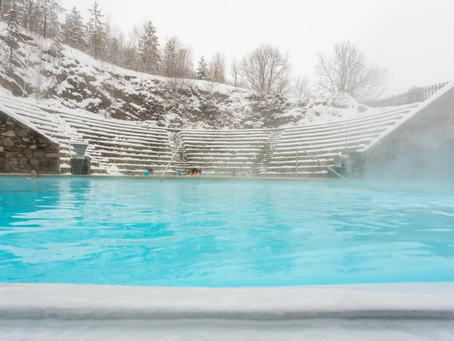 Bassin extérieur des bains de Saint-Thomas-les-Bains entouré de neige, avec des baigneurs profitant des eaux chaudes naturelles en hiver.