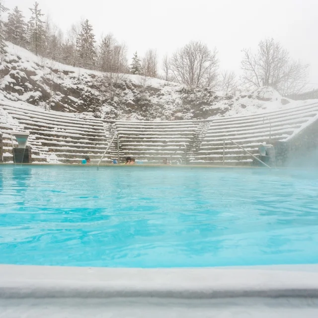 Bassin extérieur des bains de Saint-Thomas-les-Bains entouré de neige, avec des baigneurs profitant des eaux chaudes naturelles en hiver.