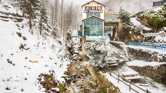 Établissement thermal de Saint-Thomas-les-Bains entouré de neige, au bord d’un ruisseau de montagne dans les Pyrénées catalanes.