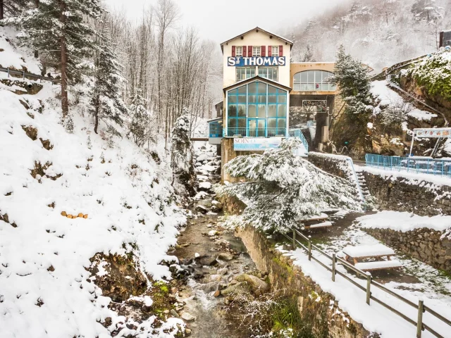 Établissement thermal de Saint-Thomas-les-Bains entouré de neige, au bord d’un ruisseau de montagne dans les Pyrénées catalanes.