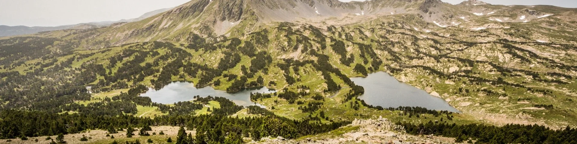 Vue panoramique sur les lacs et les reliefs du massif du Carlit, dans les Pyrénées catalanes, sous un ciel légèrement voilé.