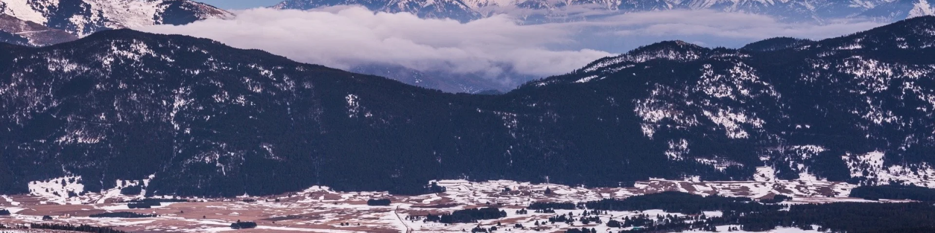 Vue panoramique sur la vallée enneigée de Cerdagne et les sommets des Pyrénées-Orientales sous un ciel aux teintes rosées du crépuscule.