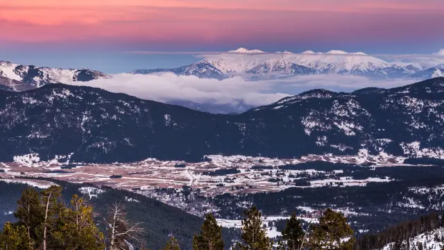 Vue panoramique sur la vallée enneigée de Cerdagne et les sommets des Pyrénées-Orientales sous un ciel aux teintes rosées du crépuscule.
