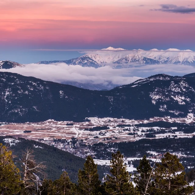 Vue panoramique sur la vallée enneigée de Cerdagne et les sommets des Pyrénées-Orientales sous un ciel aux teintes rosées du crépuscule.