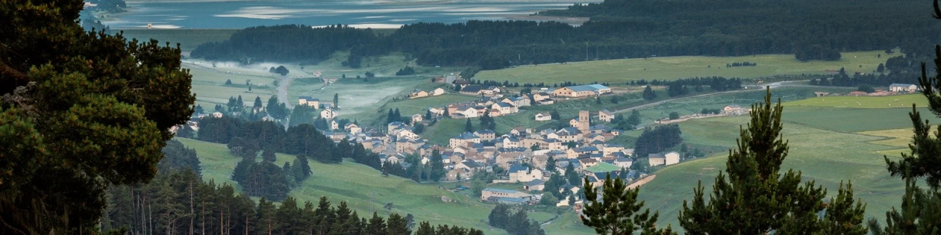 Vue panoramique sur un village de montagne entouré de forêts et de prairies verdoyantes, au lever du jour, dans la région du Capcir.