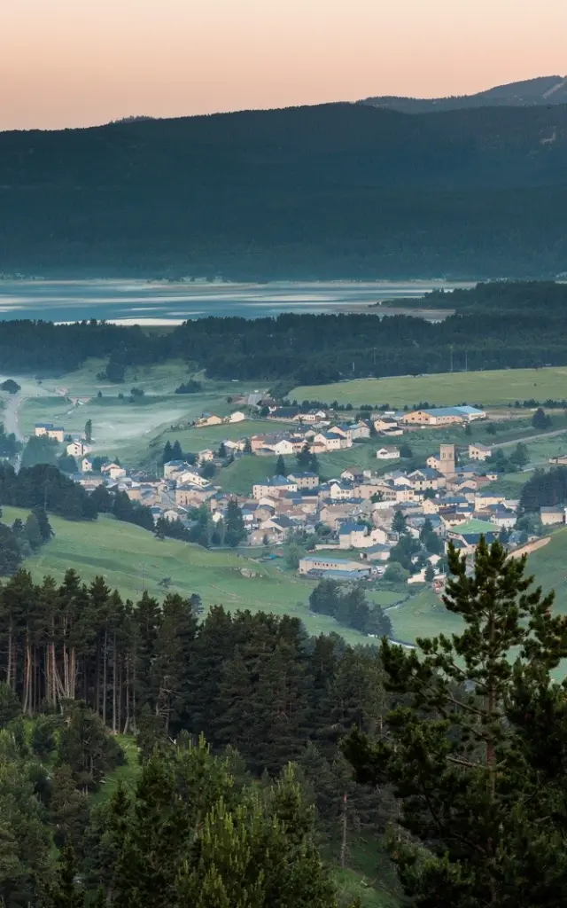 Vue panoramique sur un village de montagne entouré de forêts et de prairies verdoyantes, au lever du jour, dans la région du Capcir.