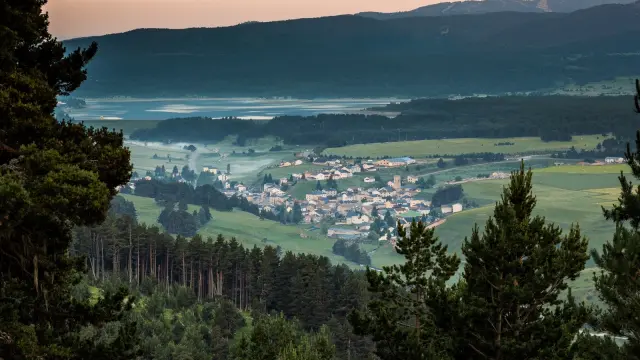 Vue panoramique sur un village de montagne entouré de forêts et de prairies verdoyantes, au lever du jour, dans la région du Capcir.