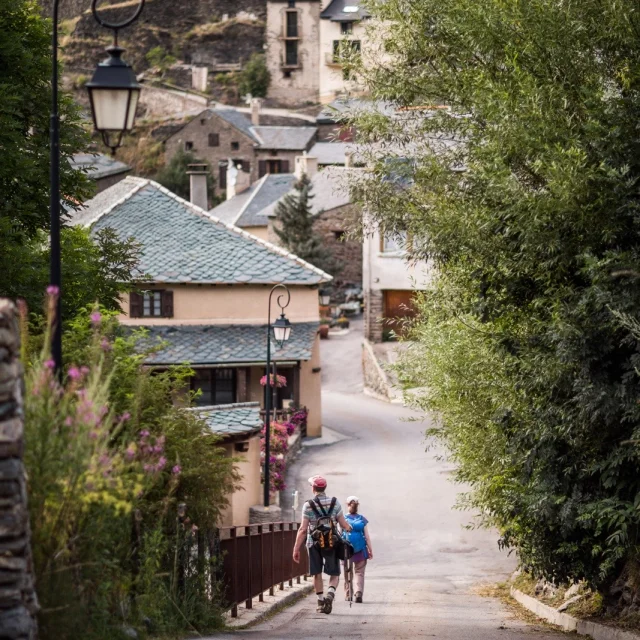 Deux randonneurs descendant une ruelle bordée de maisons en pierre dans un village de montagne des Pyrénées-Orientales.