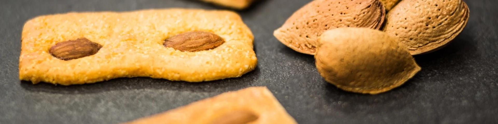 Biscuits catalans aux amandes disposés sur une surface sombre, accompagnés de quelques amandes entières en coque.