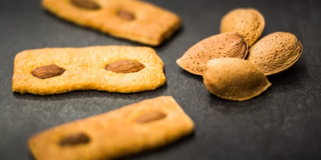 Biscuits catalans aux amandes disposés sur une surface sombre, accompagnés de quelques amandes entières en coque.
