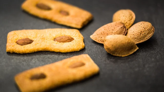 Biscuits catalans aux amandes disposés sur une surface sombre, accompagnés de quelques amandes entières en coque.