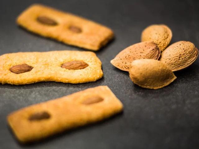Biscuits catalans aux amandes disposés sur une surface sombre, accompagnés de quelques amandes entières en coque.