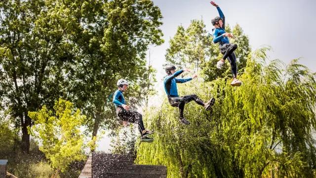 Trois personnes en combinaison et casque sautant en même temps d’une plateforme au-dessus de l’eau lors d’une activité aquatique de plein air.