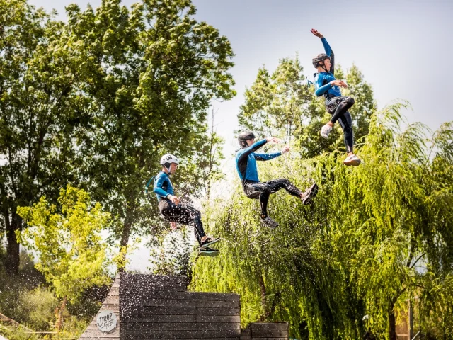 Trois personnes en combinaison et casque sautant en même temps d’une plateforme au-dessus de l’eau lors d’une activité aquatique de plein air.