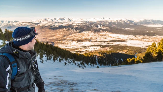 Homme équipé pour la montagne observant un panorama enneigé sur les hauts plateaux des Pyrénées catalanes, sous un ciel bleu d’hiver.