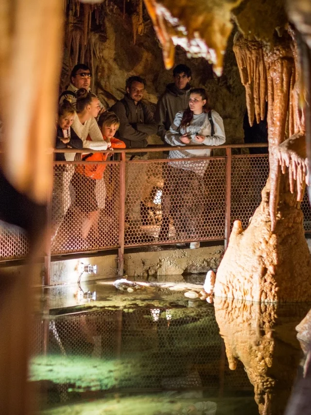 Groupe de visiteurs observant les formations rocheuses et un bassin d’eau claire lors d’une visite guidée dans une grotte.