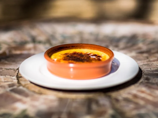 Crème catalane dorée au caramel, servie dans un ramequin en terre cuite posé sur une assiette blanche.