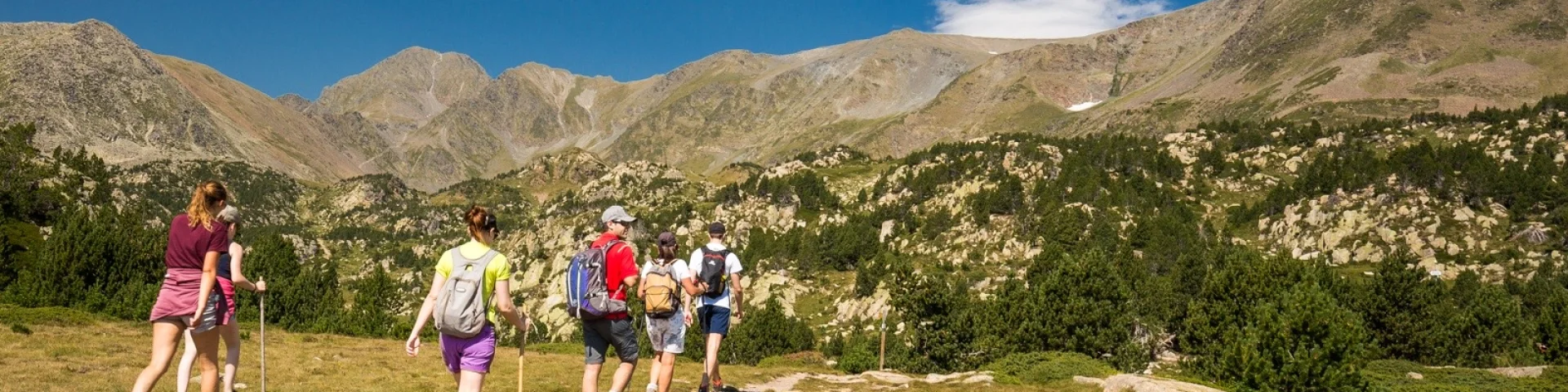 Groupe de randonneurs sur un sentier de montagne, marchant sous un ciel bleu limpide face aux sommets du massif du Canigó.
