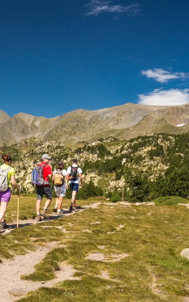 Groupe de randonneurs sur un sentier de montagne, marchant sous un ciel bleu limpide face aux sommets du massif du Canigó.