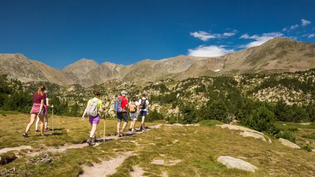 Groupe de randonneurs sur un sentier de montagne, marchant sous un ciel bleu limpide face aux sommets du massif du Canigó.
