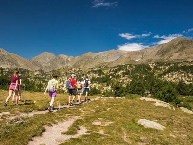Groupe de randonneurs sur un sentier de montagne, marchant sous un ciel bleu limpide face aux sommets du massif du Canigó.