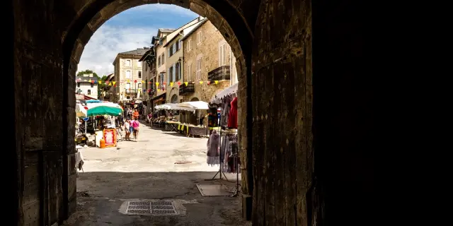 Passage voûté menant à la rue commerçante de Mont-Louis animée, avec ses étals, ses promeneurs et ses façades en pierre typiques d’une cité fortifiée.