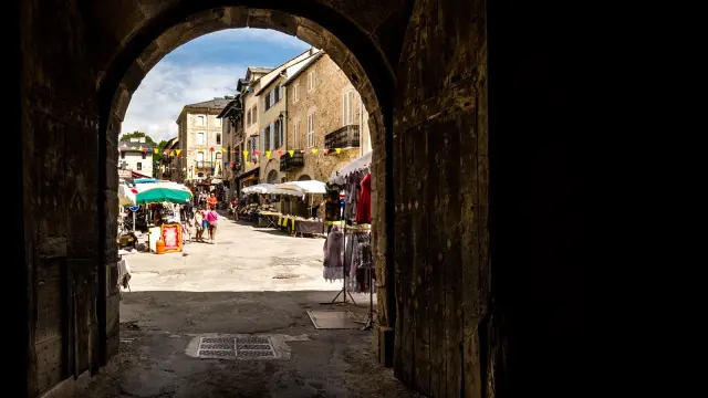 Passage voûté menant à la rue commerçante de Mont-Louis animée, avec ses étals, ses promeneurs et ses façades en pierre typiques d’une cité fortifiée.