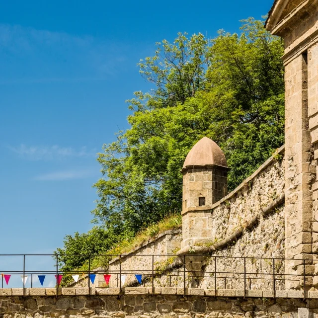 Entrée fortifiée de Mont-Louis avec sa guérite de pierre et son pont décoré de fanions colorés sous un ciel bleu d’été.