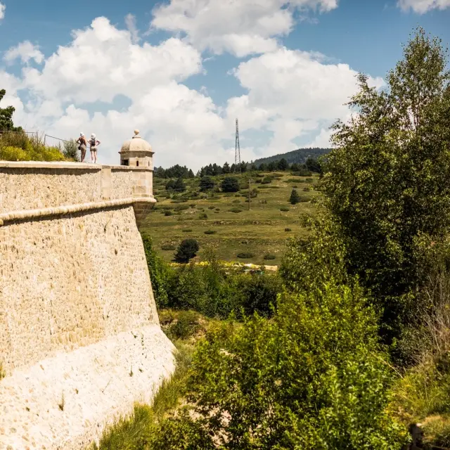 Vue d’une partie des remparts de Mont-Louis, fortification de montagne inscrite au patrimoine mondial de l’UNESCO, avec deux visiteurs observant le paysage.