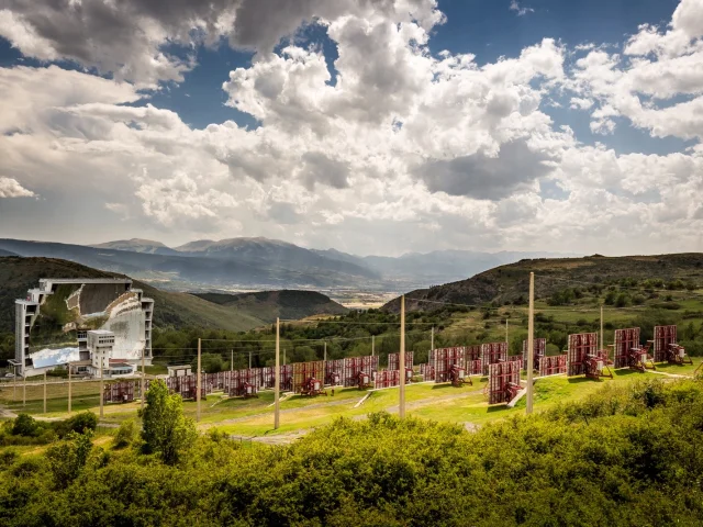 Vue du Four Solaire d’Odeillo à Font-Romeu, vaste installation scientifique composée de miroirs héliostats face à une grande parabole, avec les montagnes de Cerdagne en arrière-plan.
