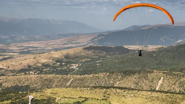 Parapentiste en vol au-dessus du Four Solaire d’Odeillo, avec vue sur les montagnes et la plaine de Cerdagne dans les Pyrénées-Orientales.